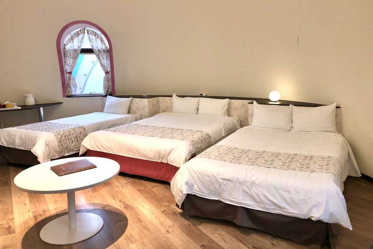 A hotel room with three beds arranged in a row, a small round table, and a window with curtains.