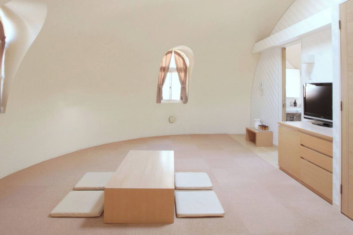 A modern interior with a curved ceiling, a central table, a small window, and a kitchenette area.