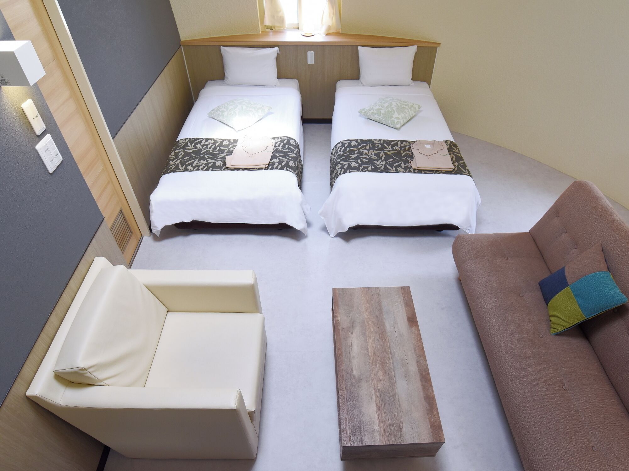 A compact room with two beds, a sofa, a small table, and a window.