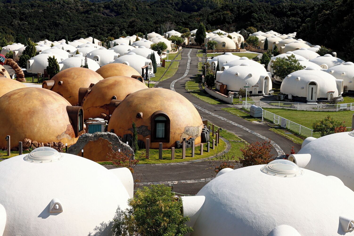 A cluster of dome-shaped buildings with a central road, surrounded by greenery.