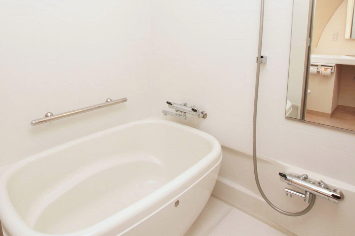 A white bathtub with a handheld showerhead, a grab bar, and a wall-mounted faucet.