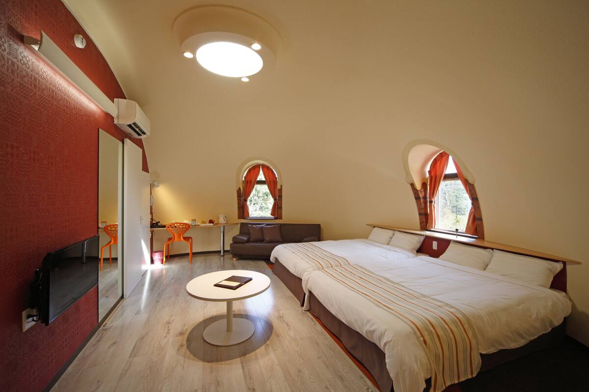 A bedroom with a large bed, a round table, and two windows with curtains.