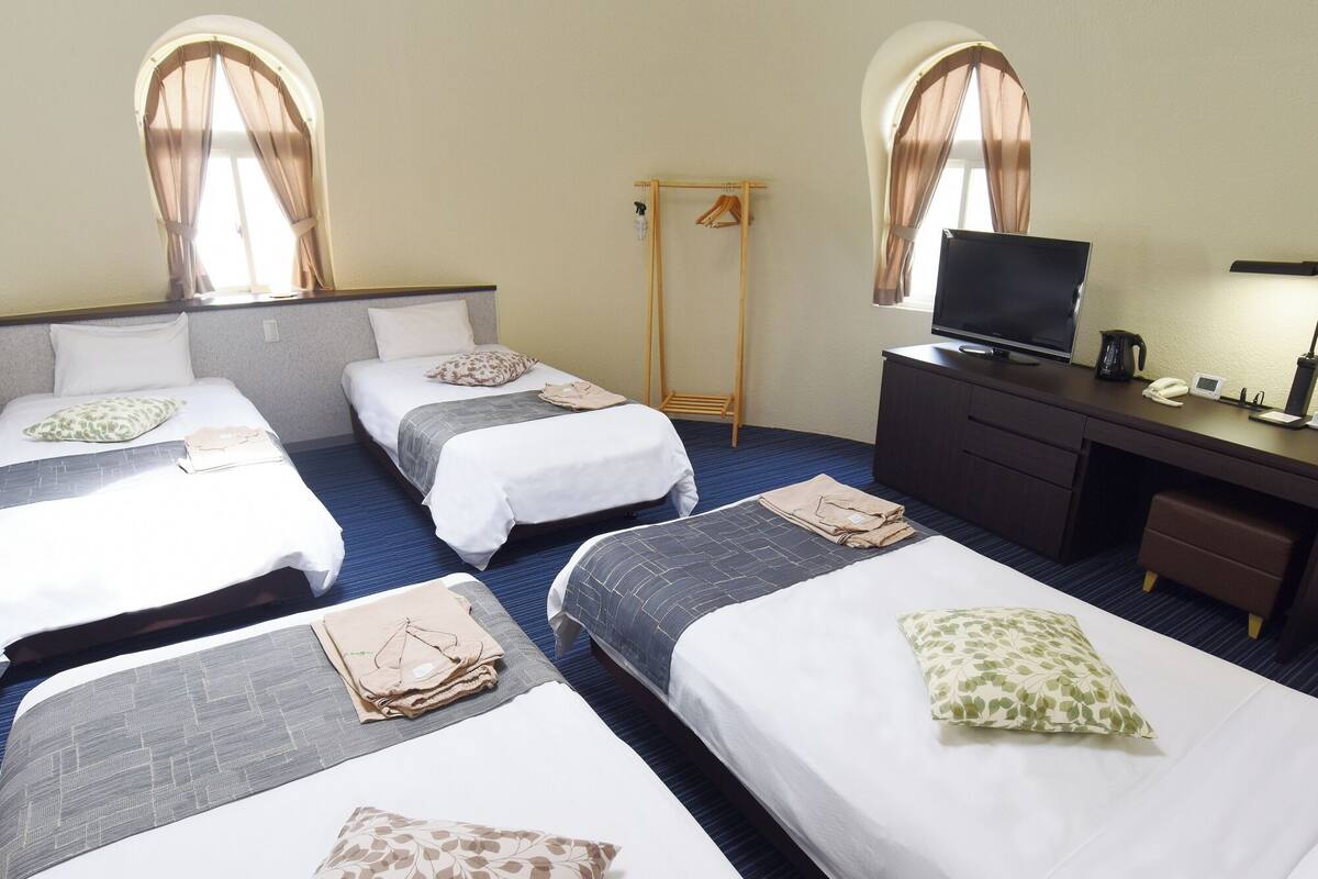 A hotel room with three beds, a desk with a TV, and a wardrobe.