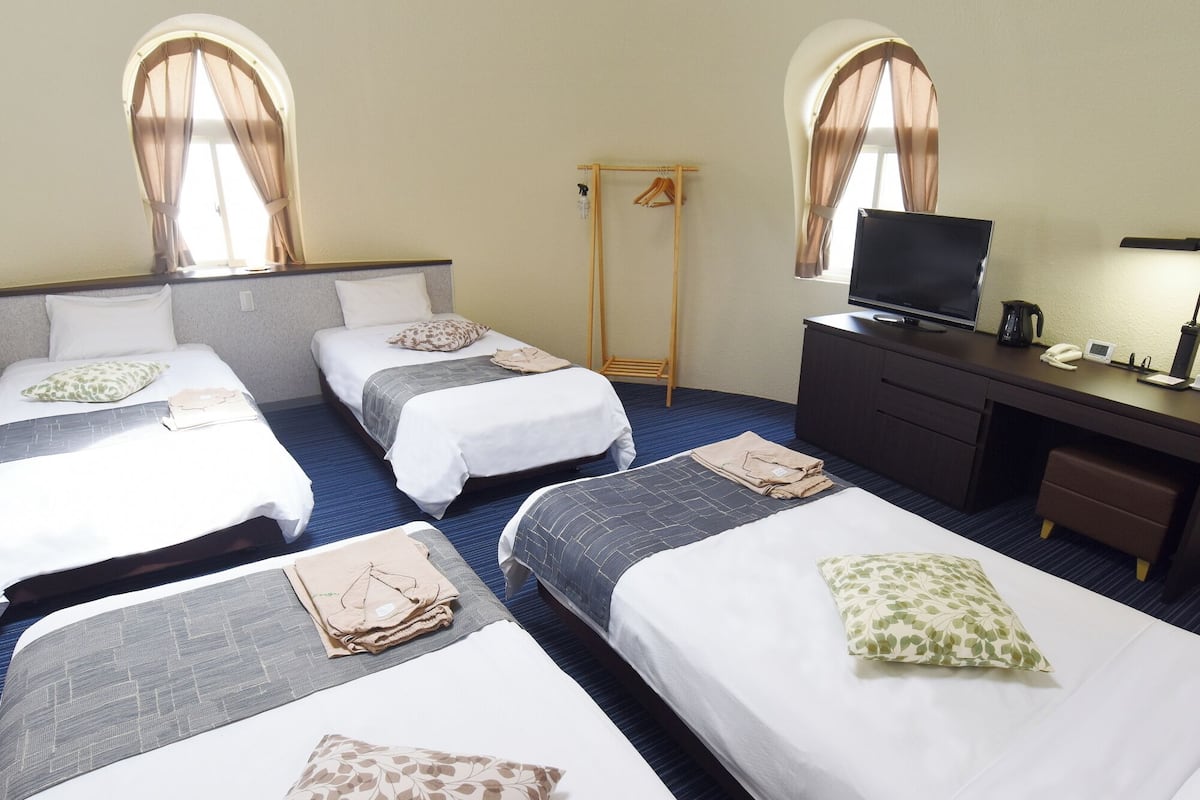 Ein Hotelzimmer mit drei Betten, einem Schreibtisch mit Fernseher und einem Kleiderschrank.
