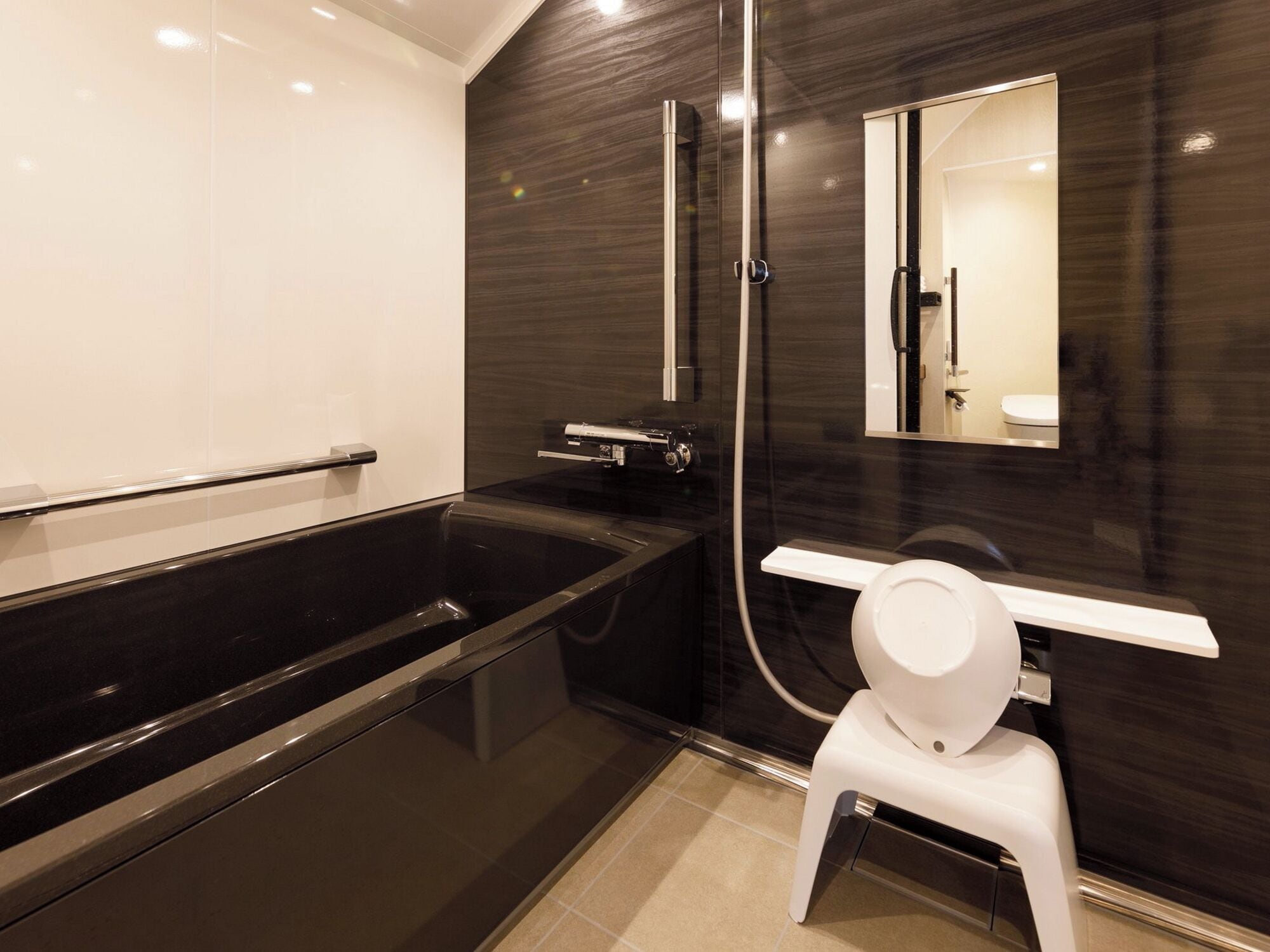 A modern bathroom with a black bathtub, a white toilet, and a mirror above the sink.