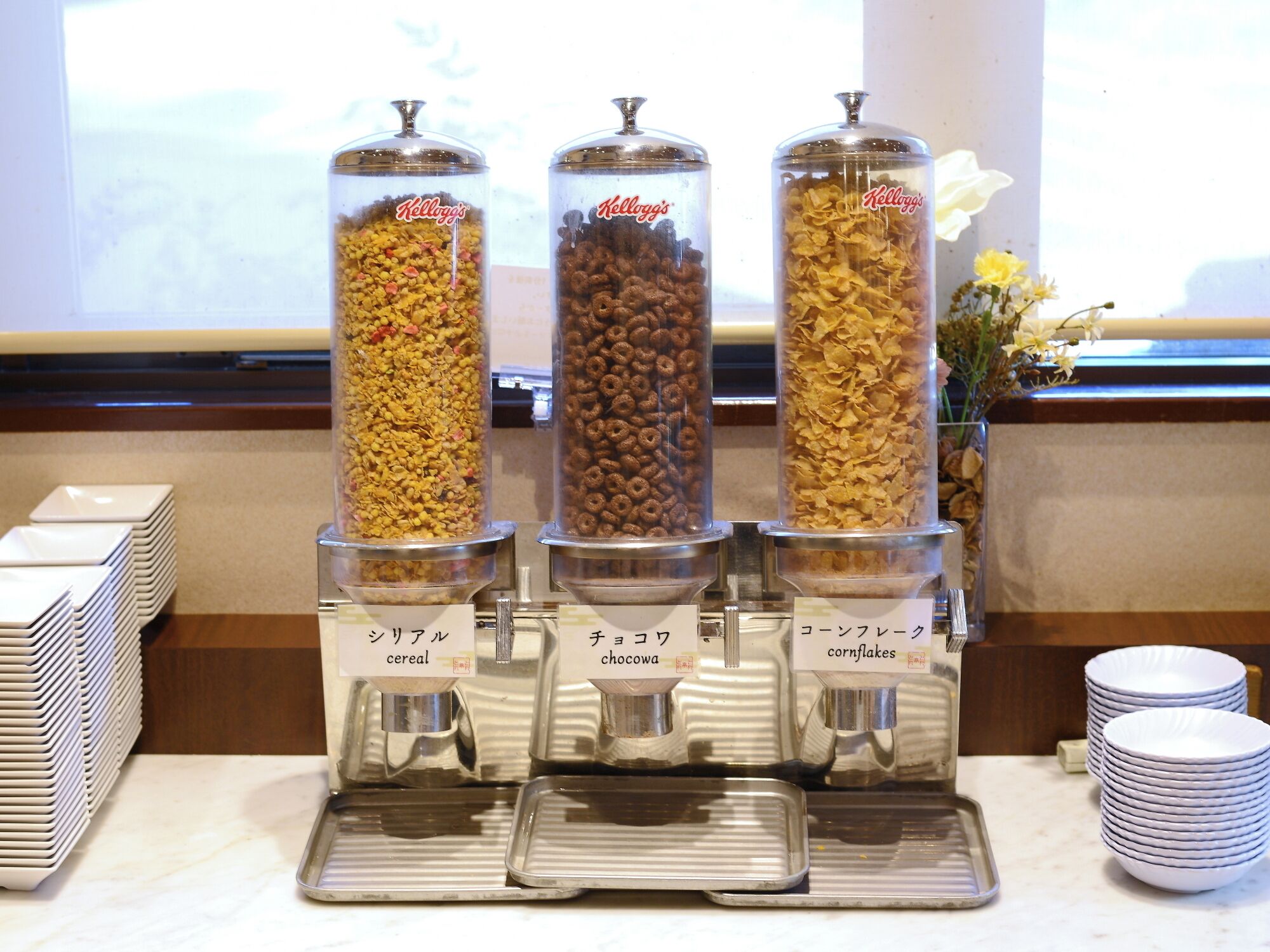 Un buffet pour le petit-déjeuner avec trois distributeurs étiquetés dans une langue étrangère, chacun contenant différents types de céréales.