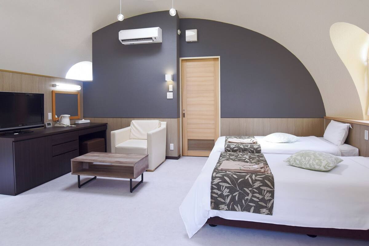 A modern hotel room with a bed, a desk, a chair, a TV, and a large mirror.