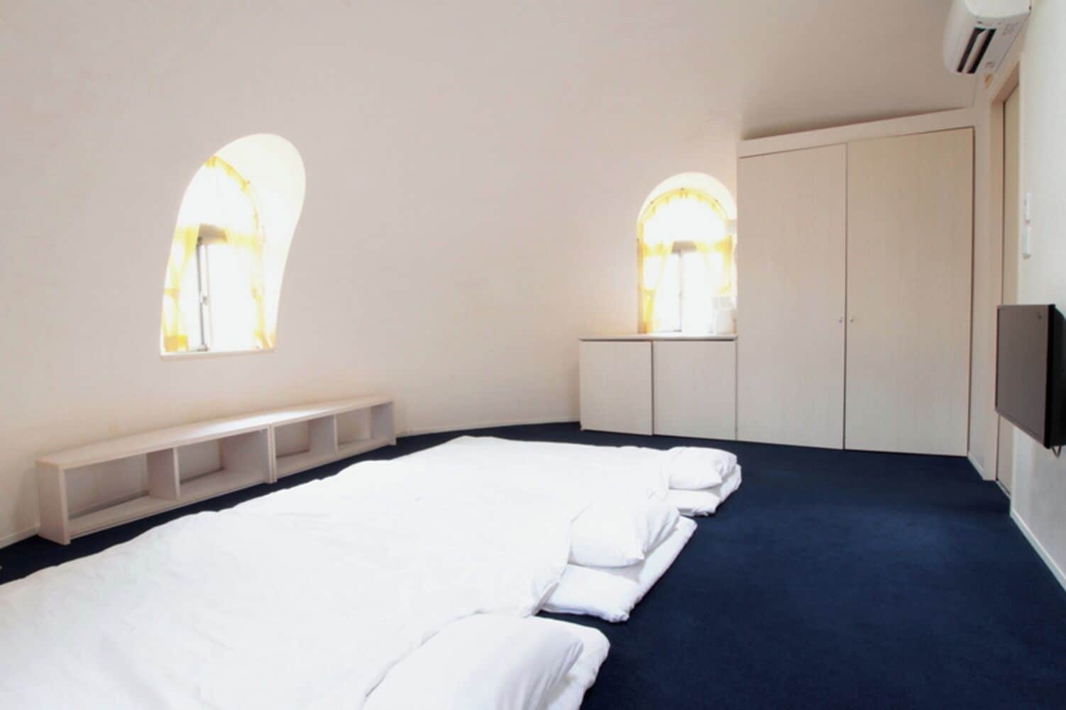 Ein Zimmer mit einem großen Bett, einer Bank, einem Kleiderschrank und zwei Rundbogenfenstern.