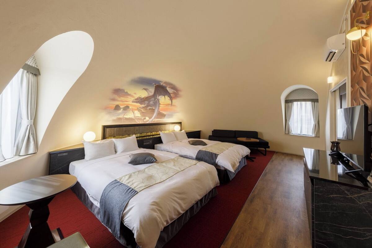 A hotel room with a large bed, a desk, a sofa, and a wall-mounted TV.