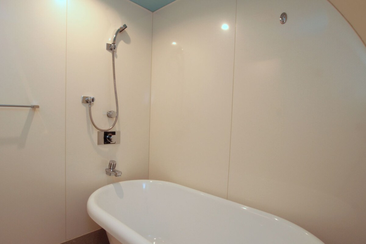 A bathroom with a white bathtub, a shower with a handheld showerhead, and a towel rack.