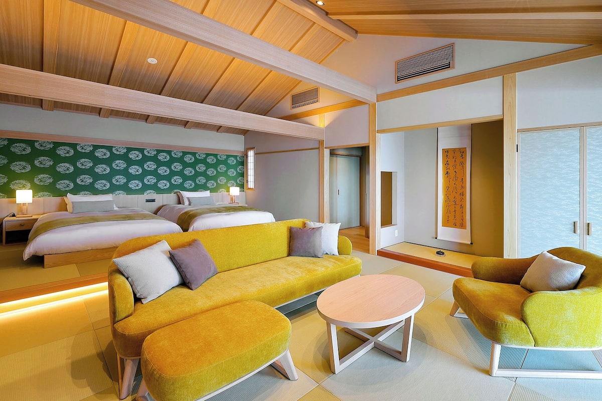 Une chambre d’hôtel comprenant un lit, deux canapés, une petite table et une porte coulissante donnant accès à une salle de bain.