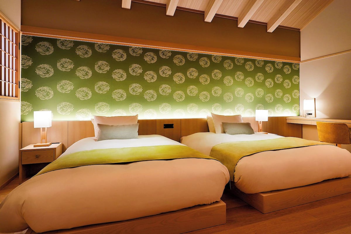 Une chambre d’hôtel avec deux lits, un bureau, une chaise, une table de chevet et une lampe.