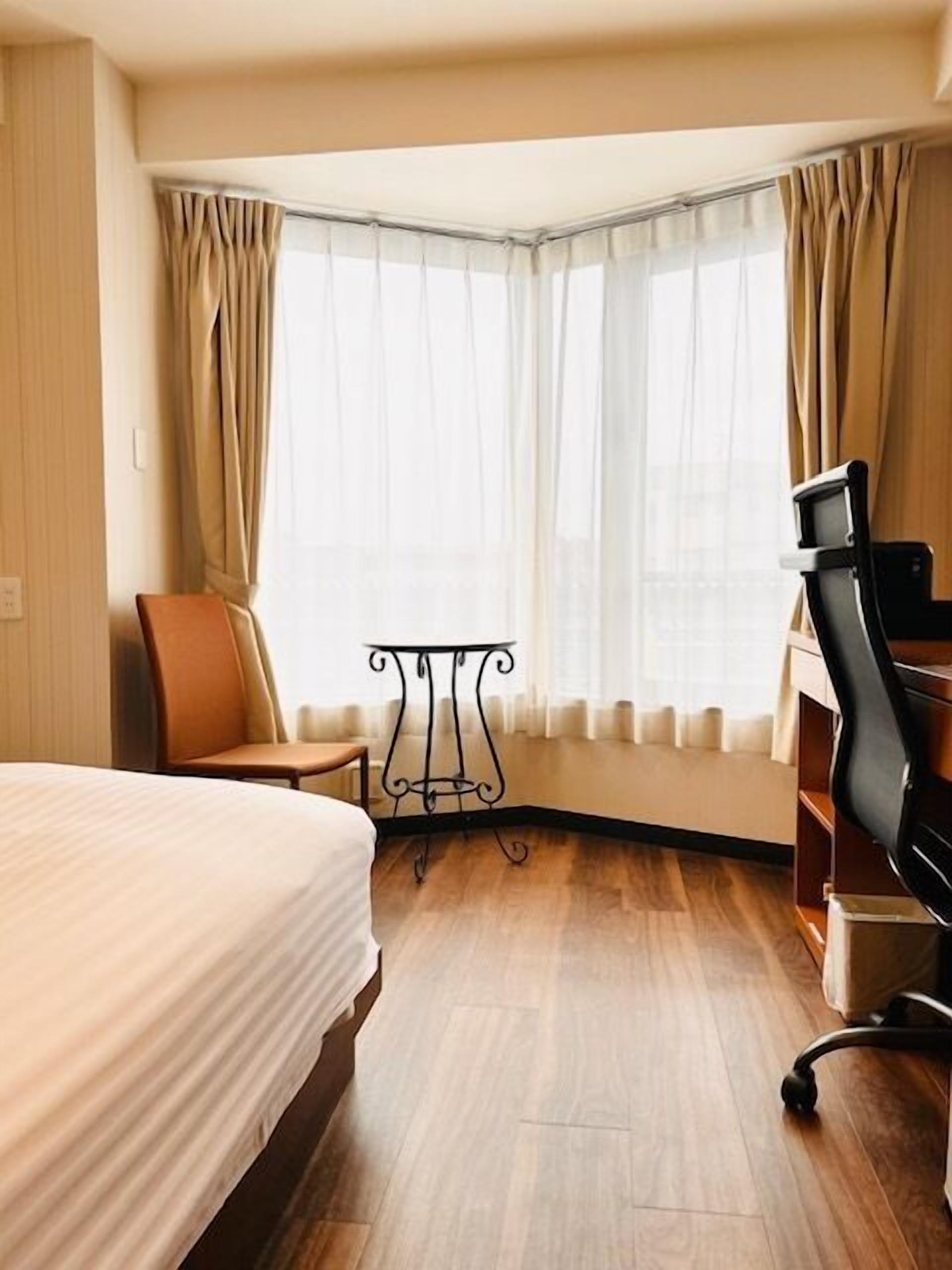 A hotel room with a bed, a desk, a chair, and a window with curtains.