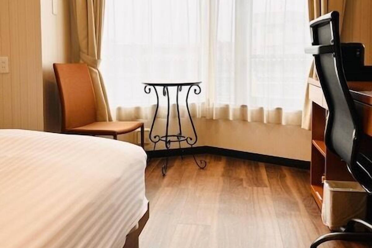 A hotel room with a bed, a desk, a chair, and a window with curtains.
