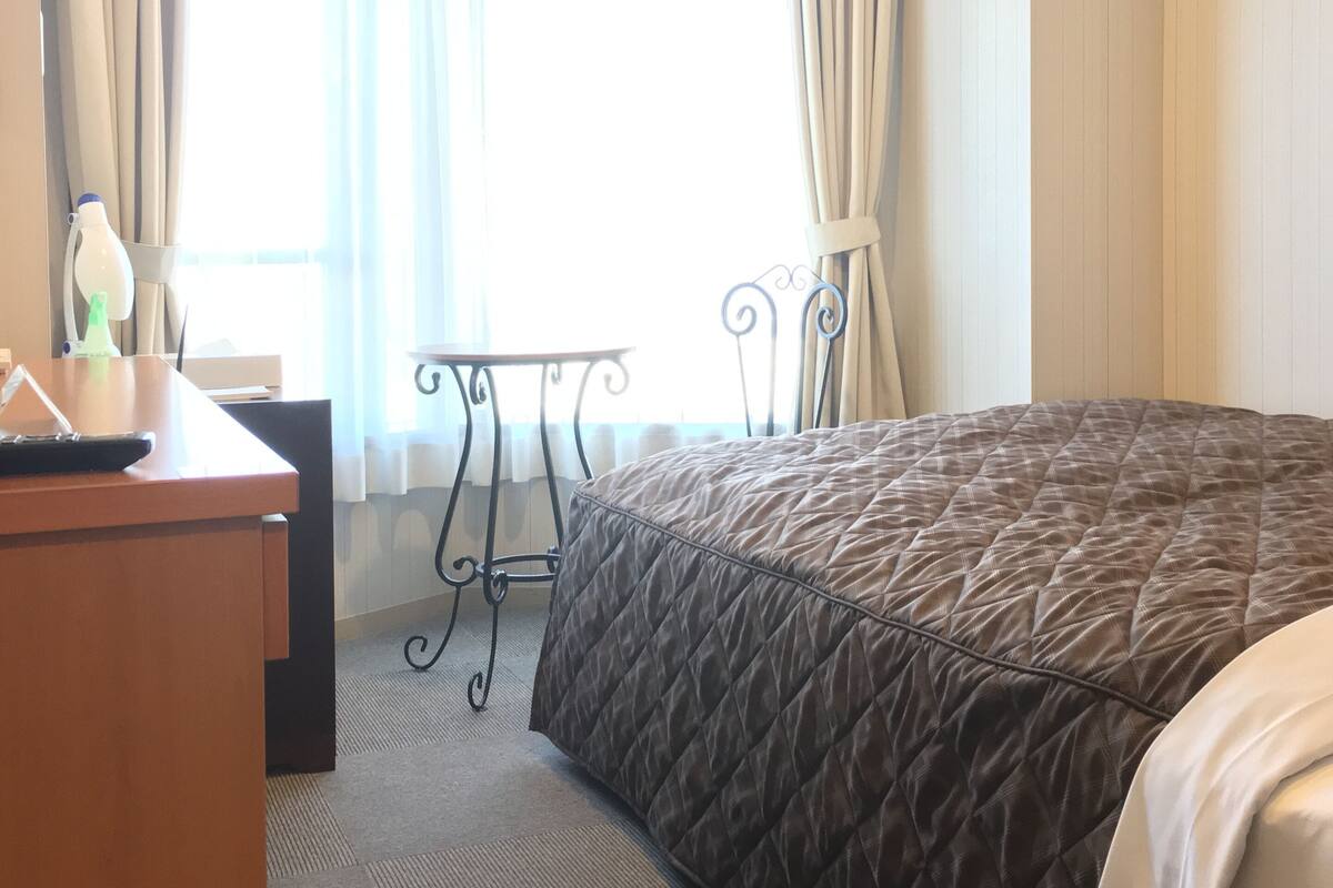 A hotel room with a large bed, a desk with a chair, a small table, and curtains on the windows.