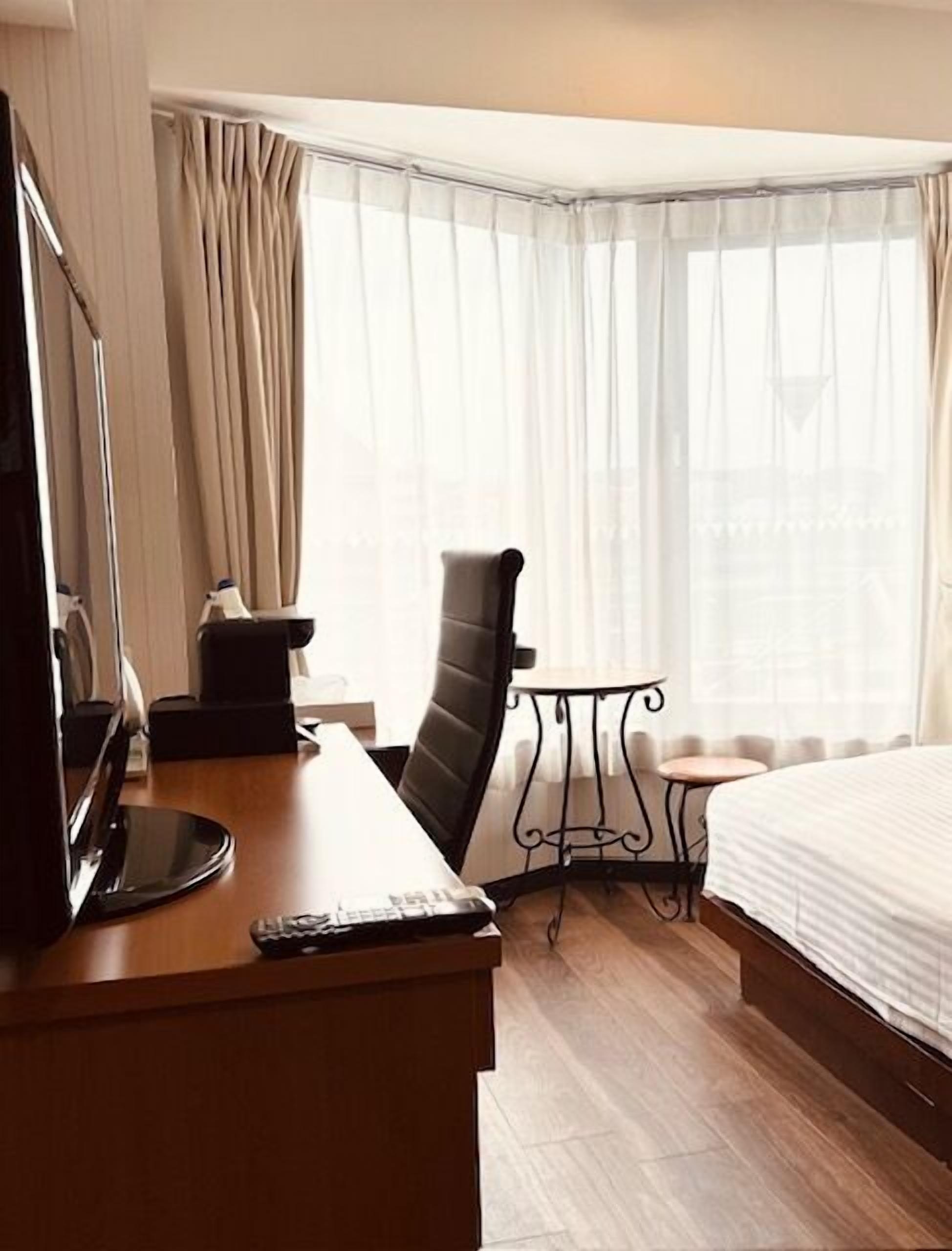 A hotel room with a desk, chair, bed, and a small table.