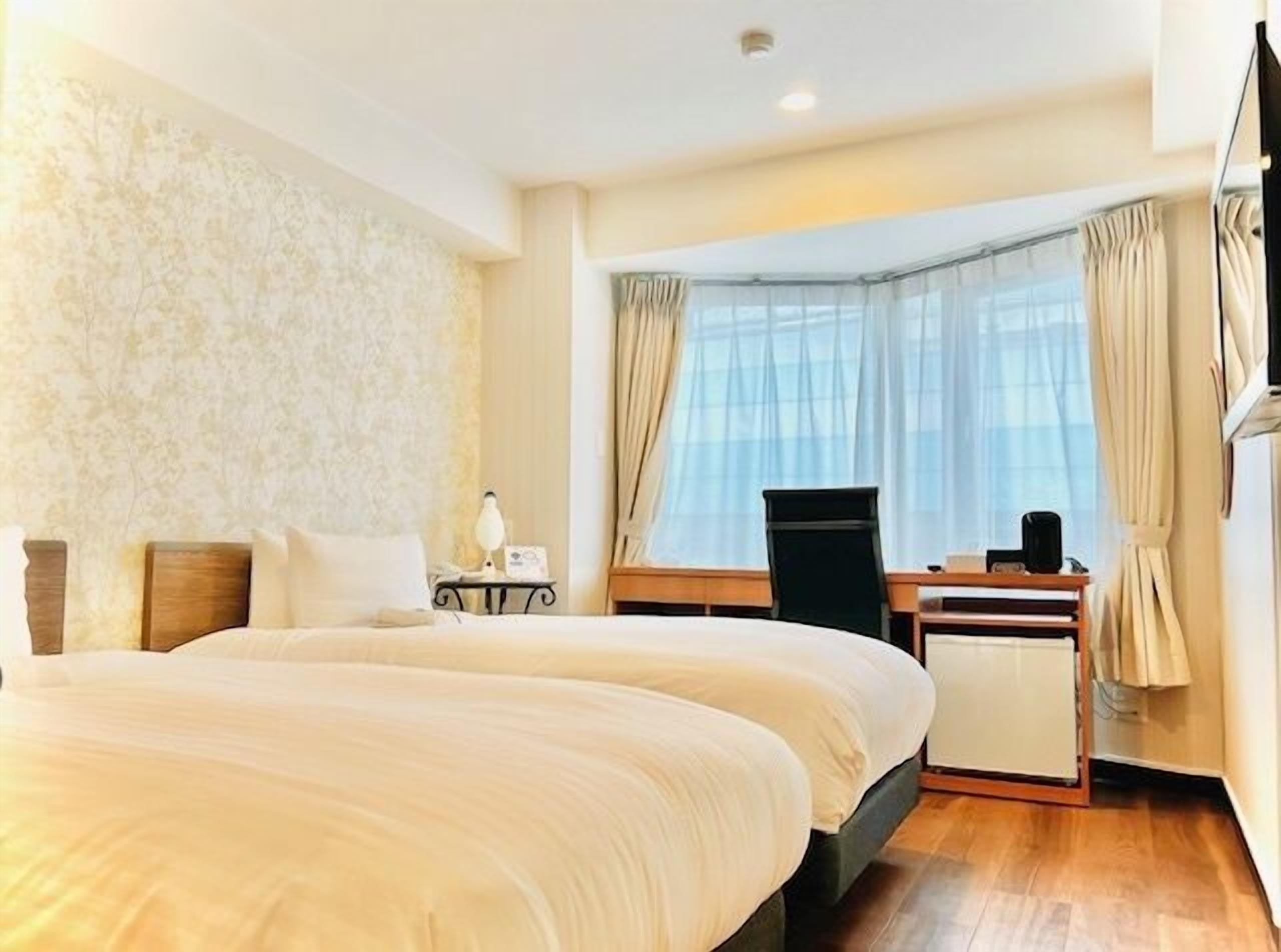 A hotel room with two beds, a desk, a chair, and a large window with curtains.