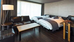 Una habitación de hotel con sofá, dos camas, un escritorio y una lámpara.