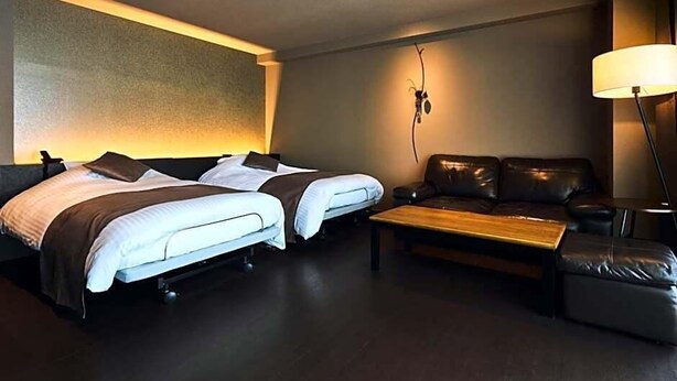 Una habitación de hotel con dos camas, un sofá, una mesa de centro y una lámpara.