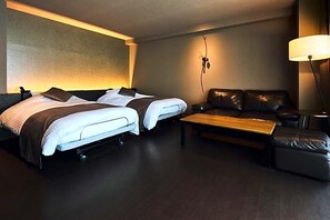 Camera d'albergo con due letti, un divano, un tavolino e una lampada.