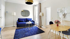 A modern room with a blue sofa, a round mirror, a wooden dining table, and a blue rug. - Superb apartment -1BR/4P- Musée d'Orsay /Louvre (Paris)
