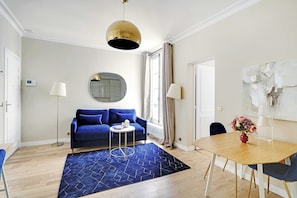 Une pièce moderne avec un canapé bleu, un miroir rond, une table à manger en bois et un tapis bleu.