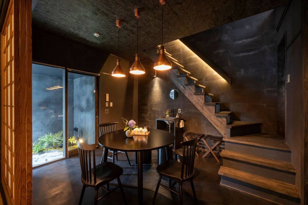 Ein modernes Interieur mit einem runden Tisch, Stühlen, Pendelleuchten, einer Treppe und Blick durch Glastüren.