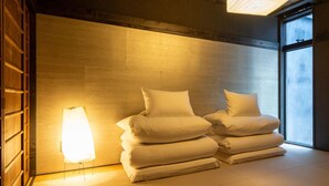 Ein Zimmer mit Tatami-Matten, einem traditionellen japanischen Bett, einer Wandleuchte und einem Fenster.