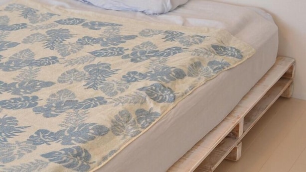Een bed met een deken met bloemenprint, een kussen en een houten bankvoet.
