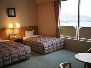 A hotel room with two beds, a nightstand, a table, and a window with a view. - Shikisainoyado Hanatsubaki (Obama)