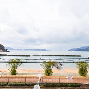 A coastal view with a sandy beach, a rocky breakwater, and distant mountains.
