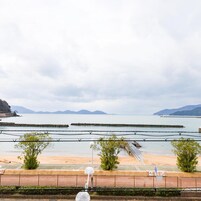Vista costera con playa arenosa, un rompeolas rocoso y montañas al fondo.