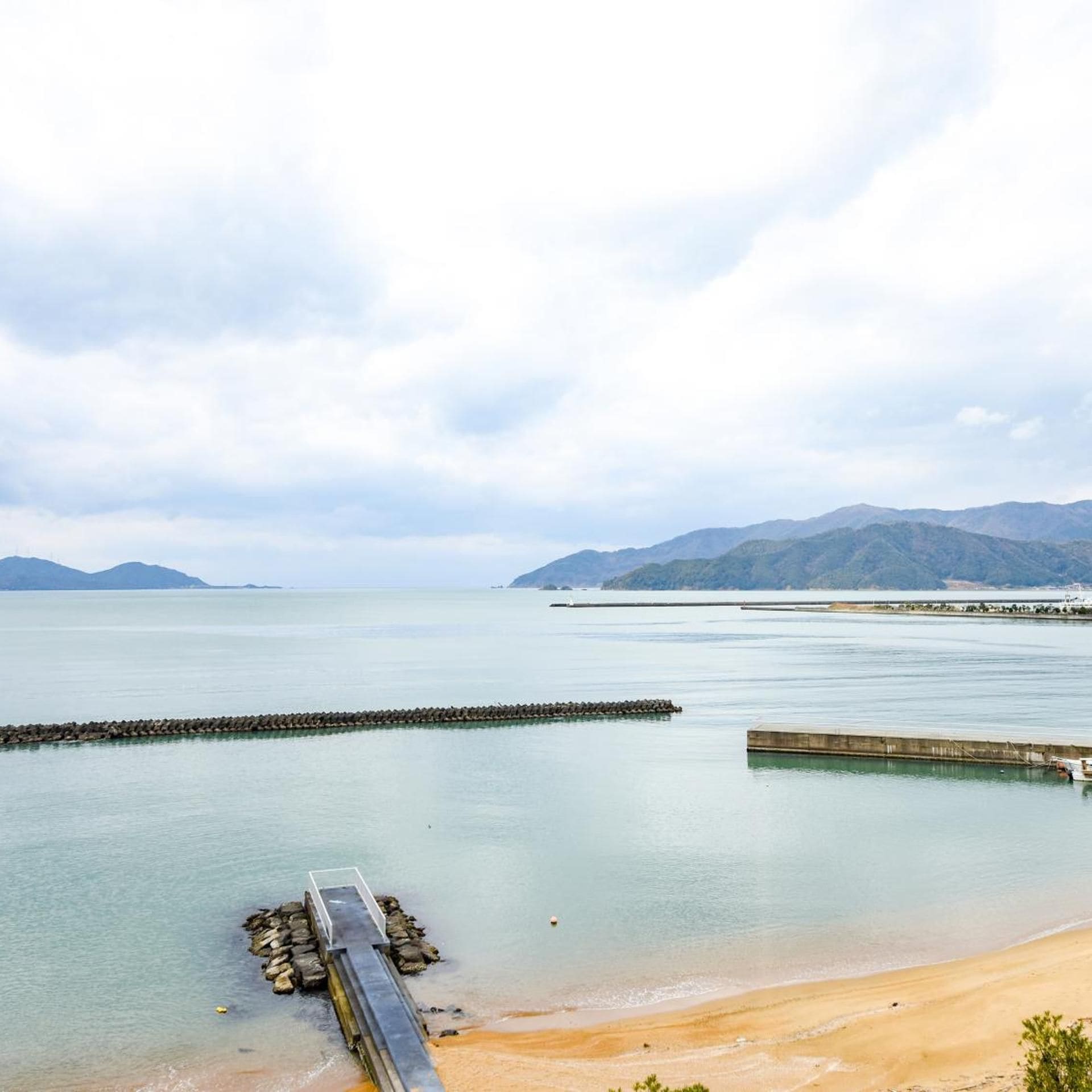 A coastal landscape with a beach, calm water, and distant mountains.