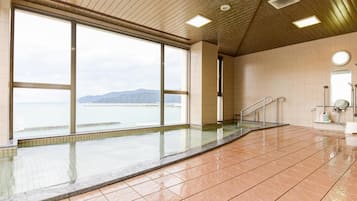 A spacious indoor swimming pool with large windows offering a view of the sea and mountains.
