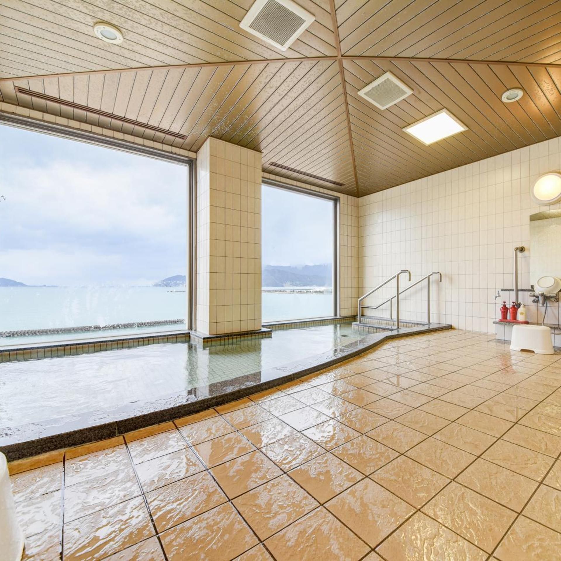 A swimming pool with a view of the sea, tiled walls, and a ceiling with recessed lighting.