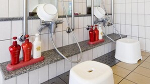 Ein Badezimmer mit drei Waschbecken, jeweils mit Spiegel und Handbrause. Seifenspender und ein weißer Hocker sind ebenfalls vorhanden.