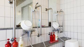 A bathroom with three sinks, each with a mirror and a handheld showerhead. There are soap dispensers and a white stool.