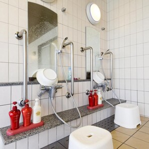 Ein Badezimmer mit drei Waschbecken, jeweils mit Spiegel und Handbrause. Seifenspender und ein weißer Hocker sind ebenfalls vorhanden.