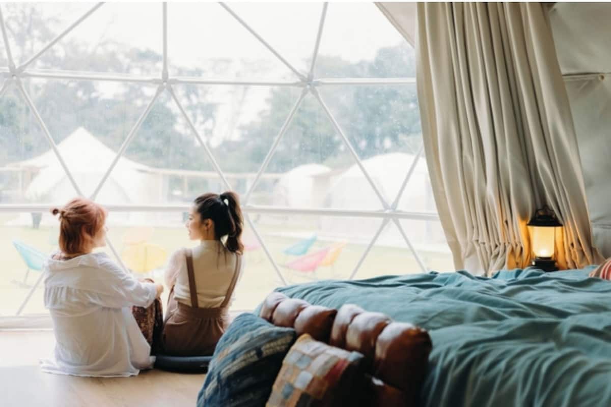 Una habitación con un ventanal grande, una cama con edredón azul y una lámpara en la mesita de noche.