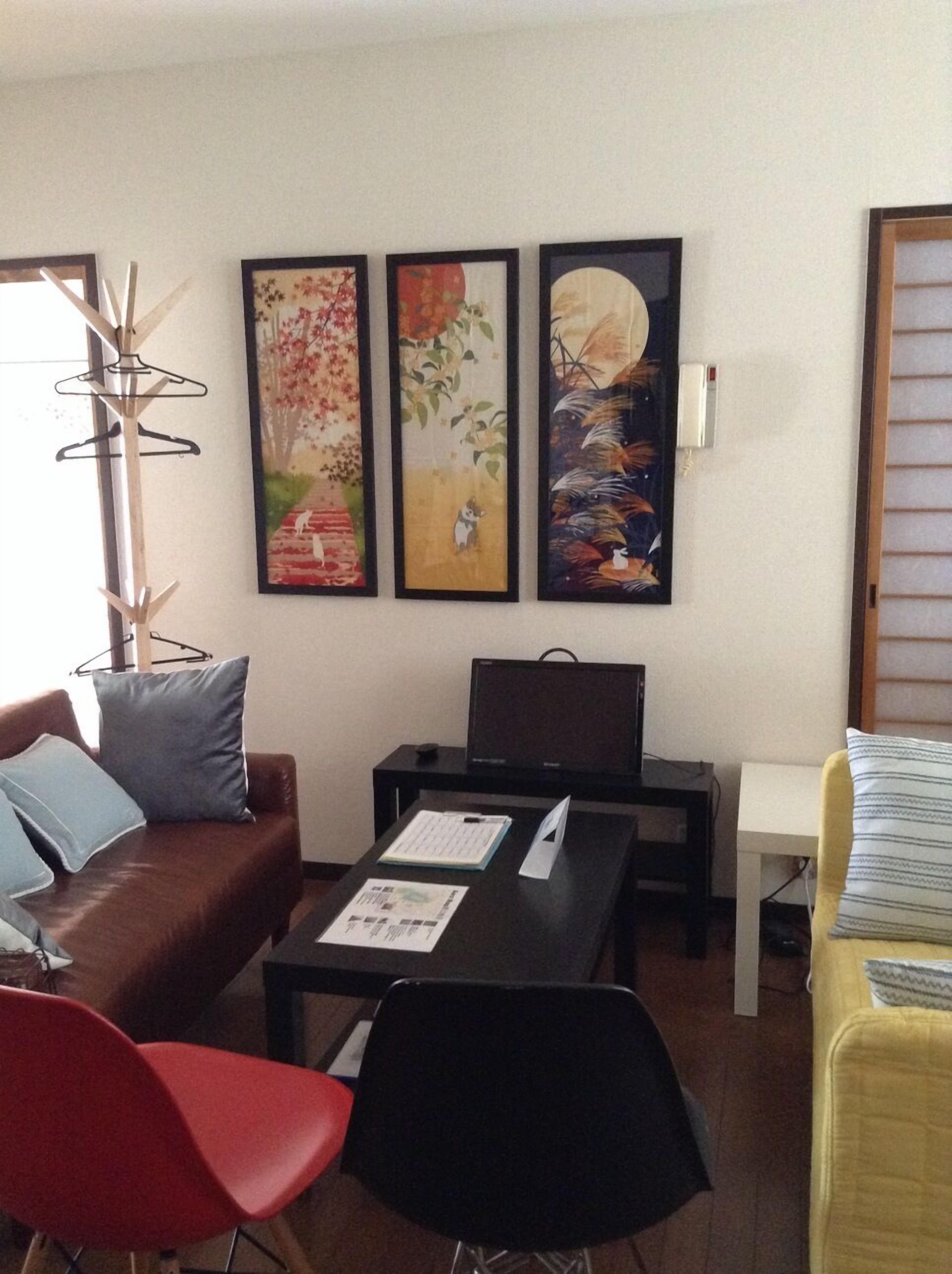 Ein Wohnzimmer mit einem braunen Ledersofa, einem roten Sessel, einem schwarzen Tisch mit einem Laptop und drei gerahmten Kunstwerken an der Wand.