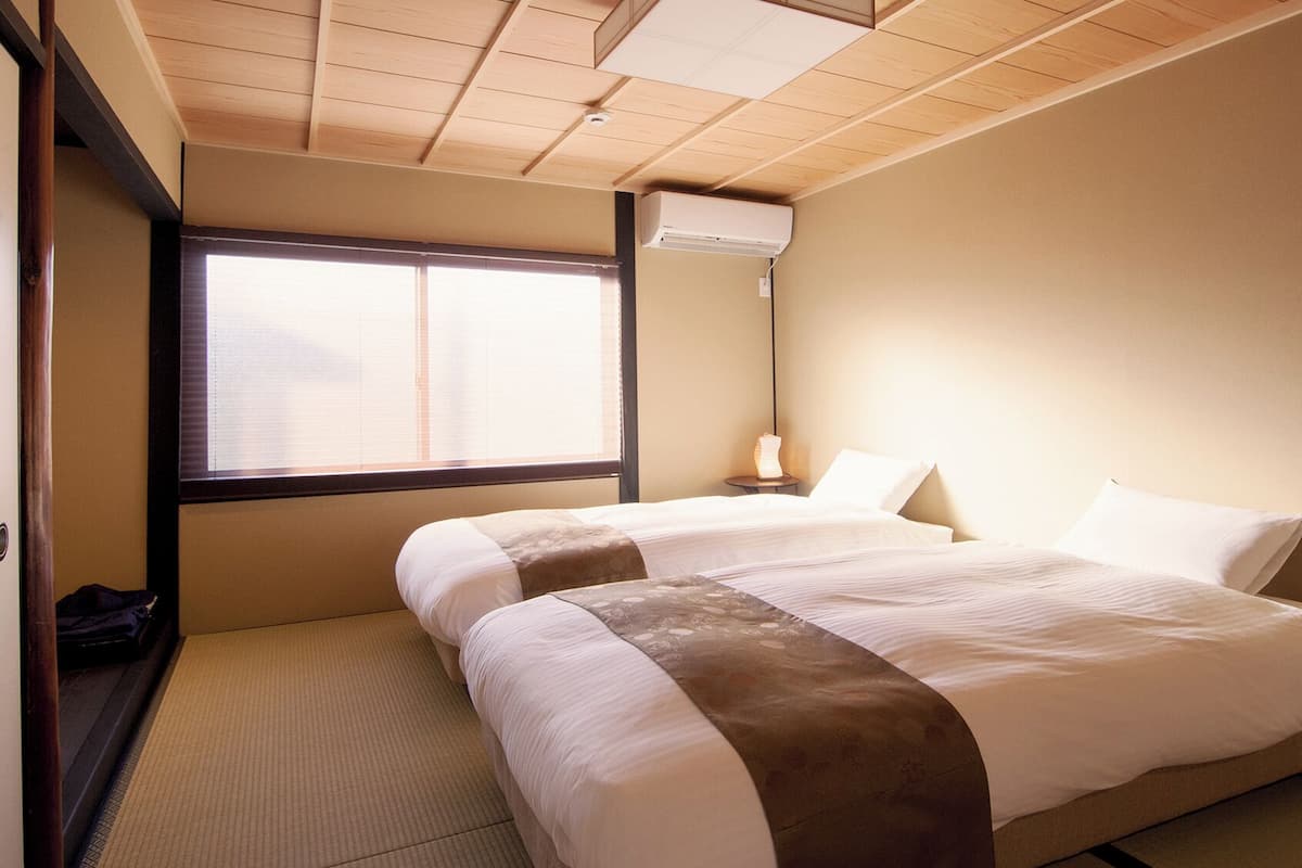 Ein Hotelzimmer mit Bett, Nachttisch, Lampe und Fenster mit Jalousien.