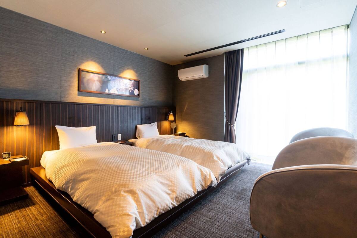 Een hotelkamer met twee bedden, een groot raam, een airconditioning en een kunstwerk aan de muur.