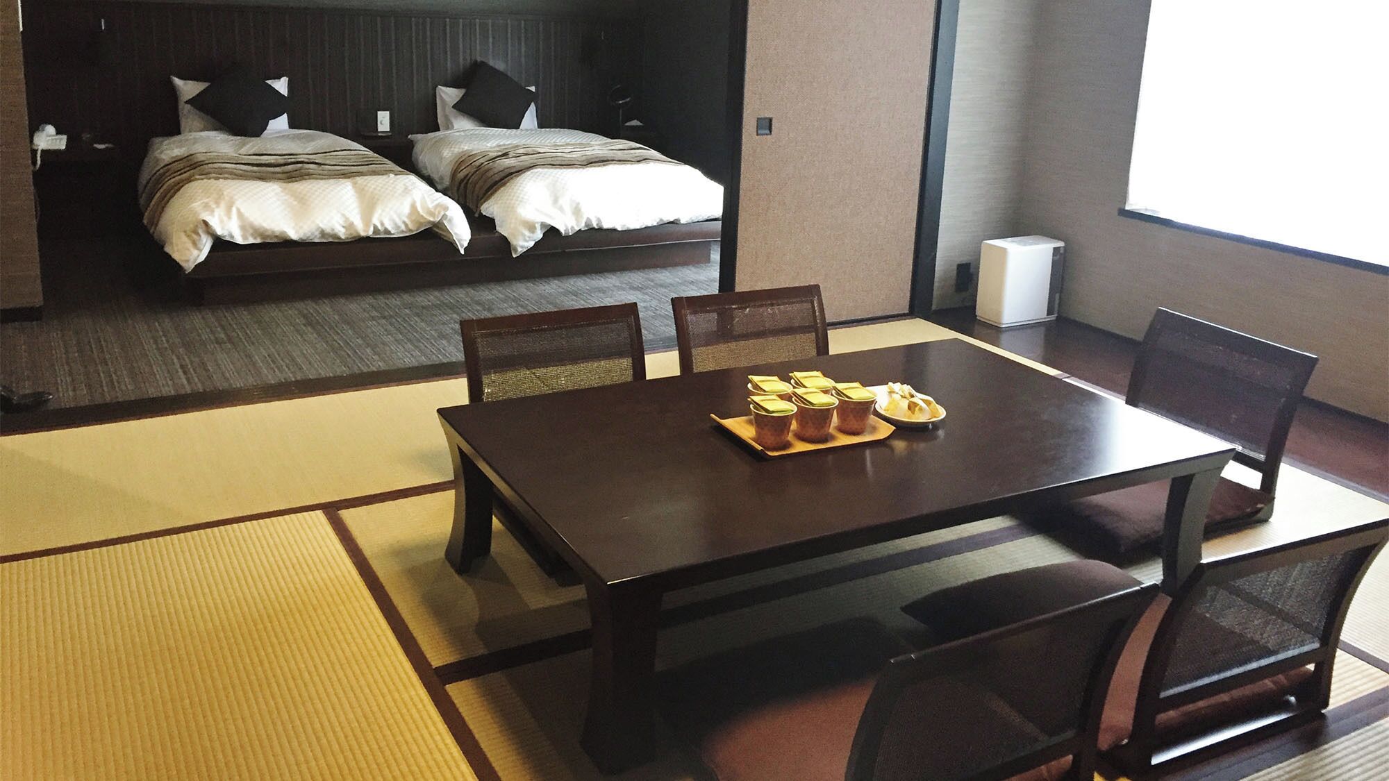 A hotel room with a bed, a dining table with chairs, and a view of the sea.