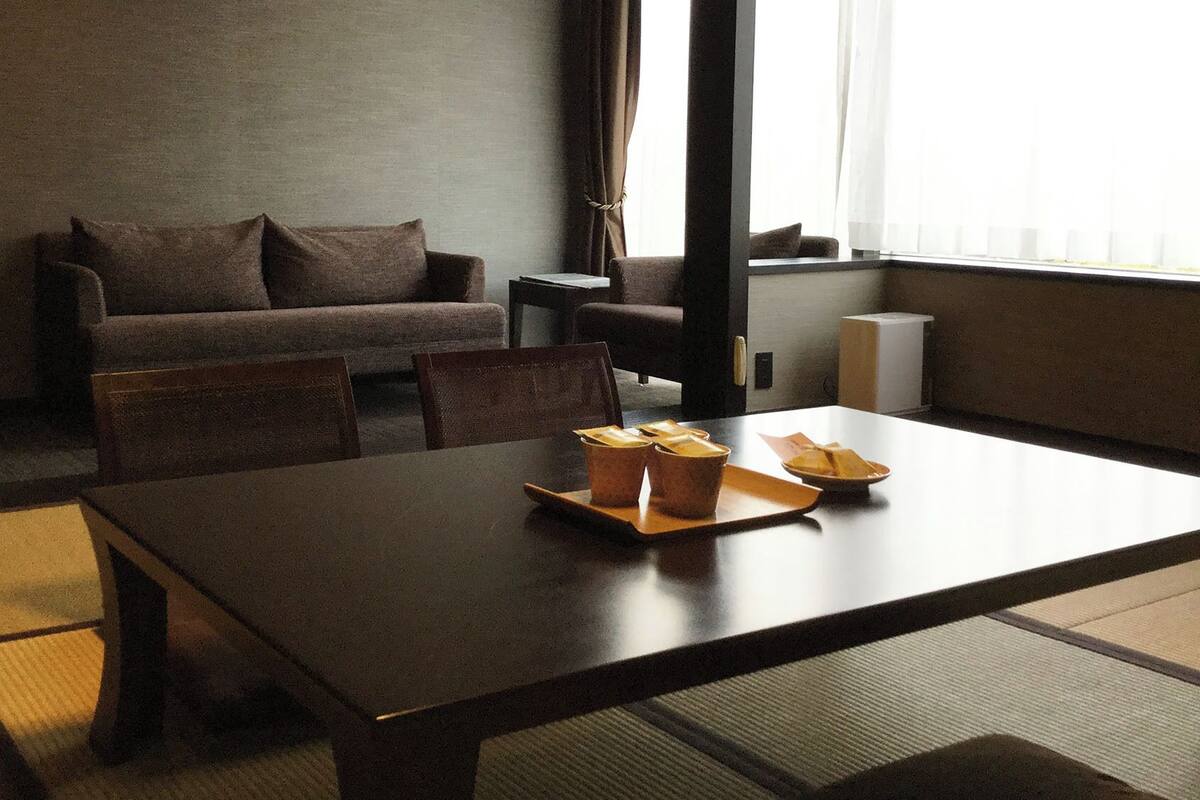 Een kamer met een donkerhouten tafel, een bank en een stoel. Op de tafel staan spullen, waaronder een dienblad en een schaal.