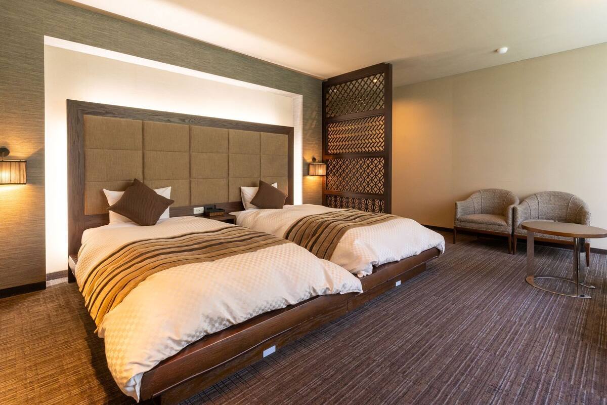 Een hotelkamer met twee bedden, een bank, een kleine tafel en een decoratieve scheidingswand.