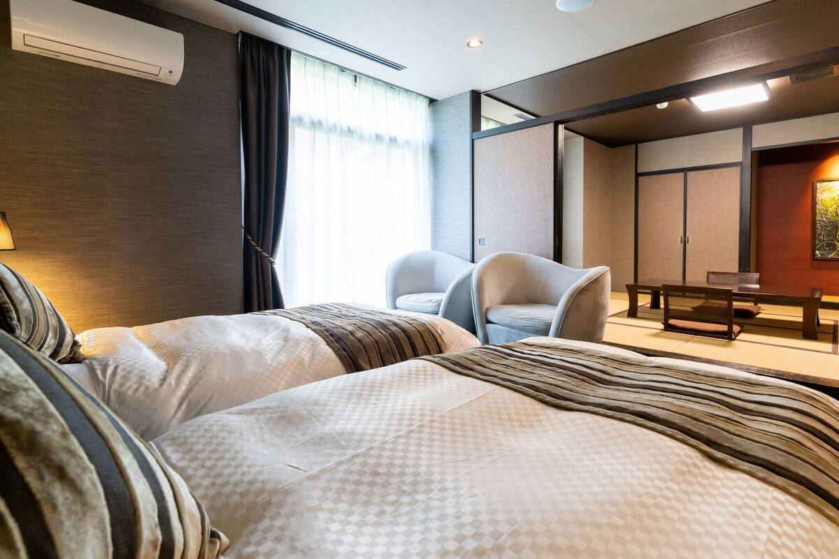 Een hotelkamer met twee bedden, een zithoek met stoelen, een tafel en een groot raam met gordijnen.