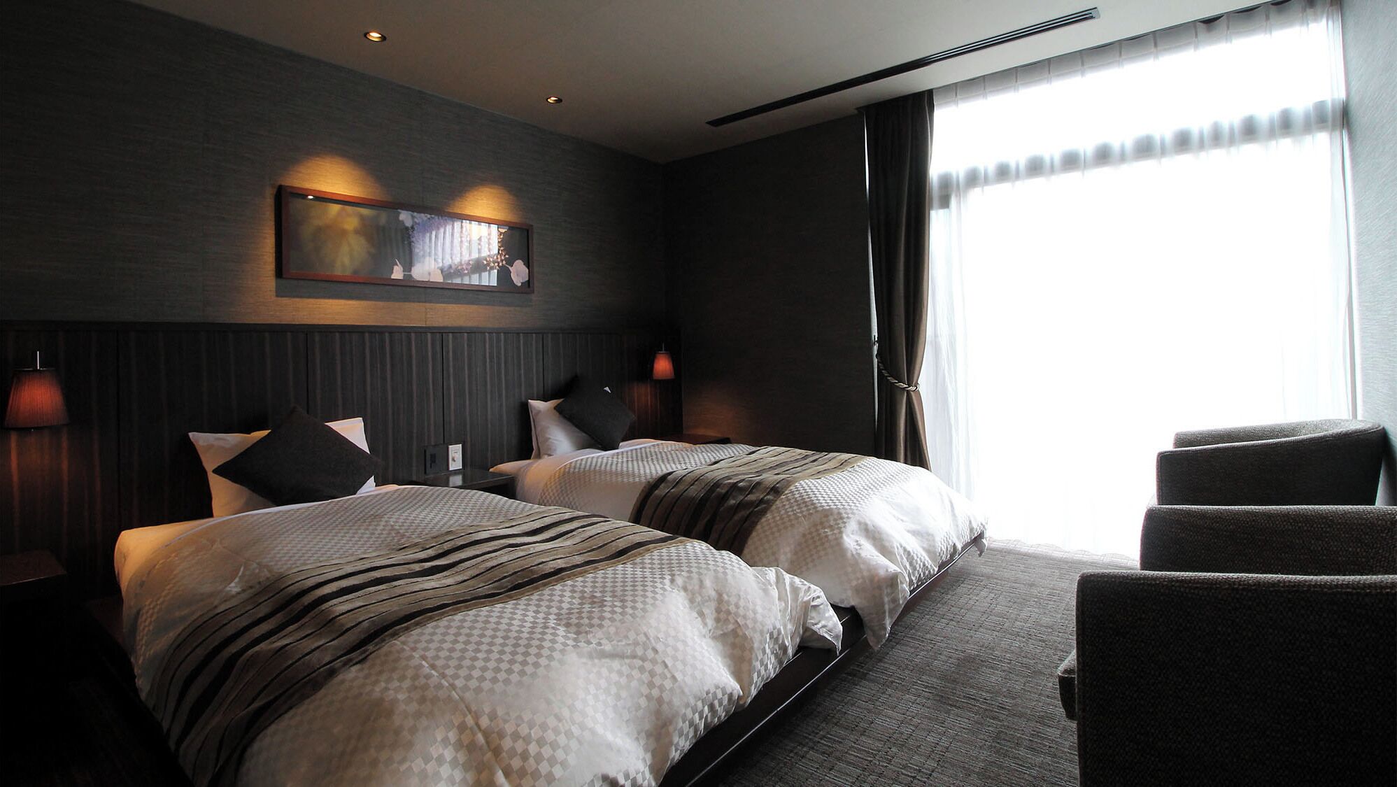 A hotel room with two beds, a large window, and a chair.