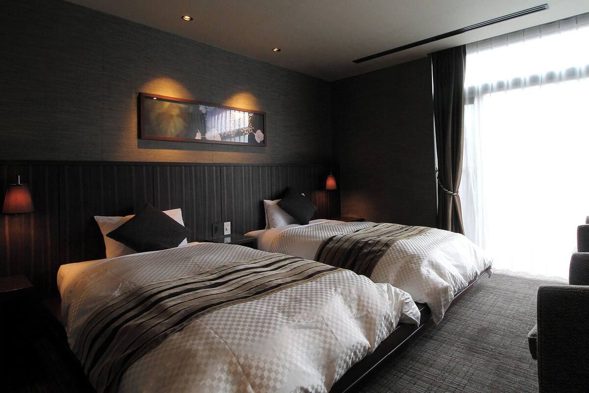 Een hotelkamer met twee bedden, een groot raam en een stoel.