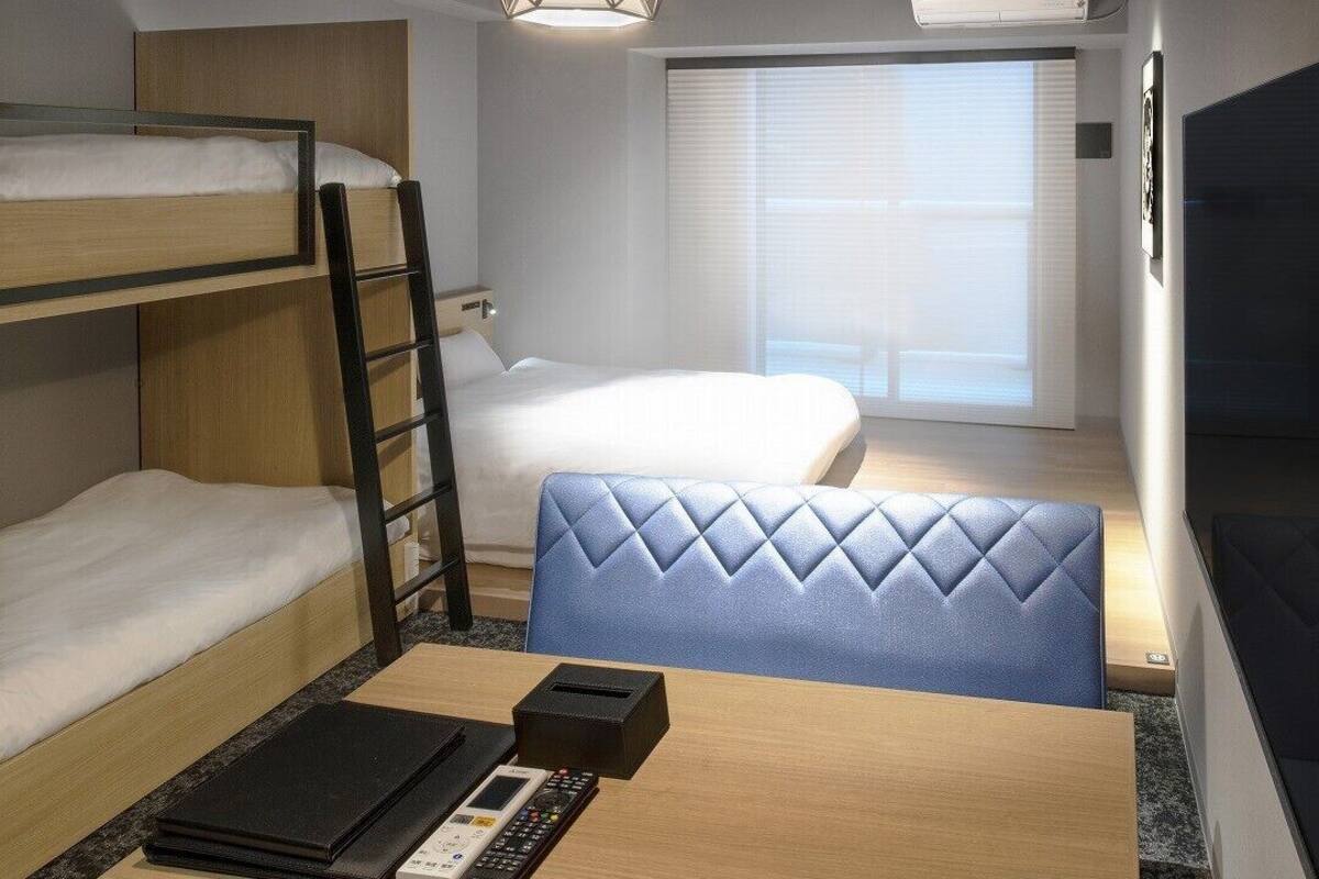 A bunk bed, a desk with a laptop, a chair, a TV, and a window with blinds.