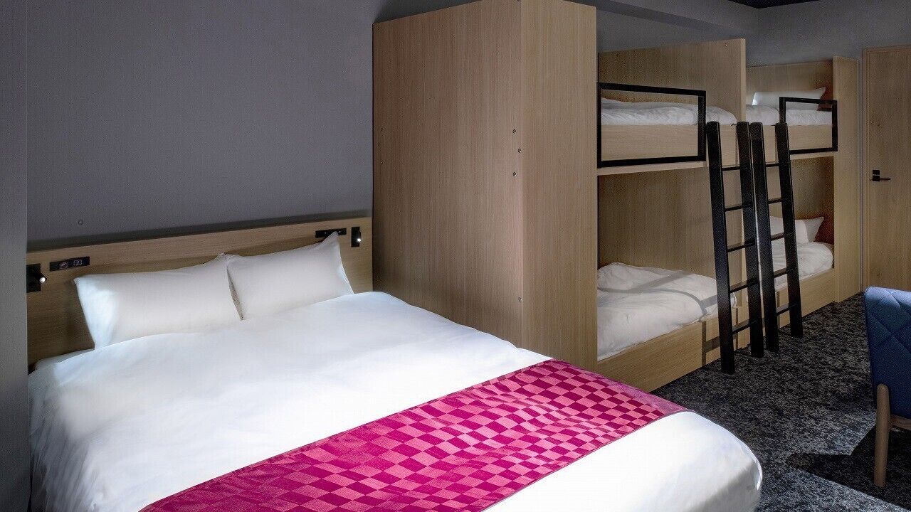 A hotel room with a single bed, a bunk bed, a desk, and a chair.